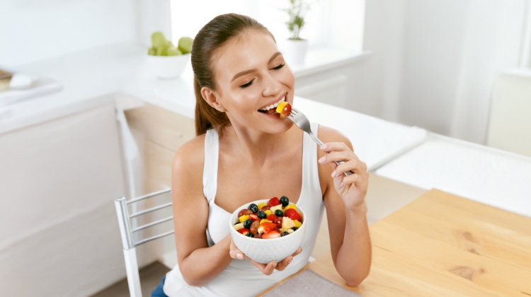 Smiling woman enjoying a fresh fruit salad, highlighting healthy eating tips for maintaining oral health during the holidays in Cottonwood, AZ.